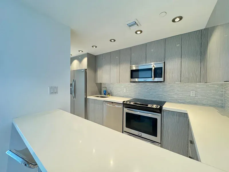 A clean kitchen with grey units, white worktops and steel appliances